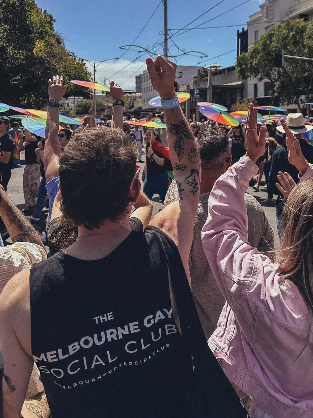Club members marching together at a Pride parade with rainbow umbrellas
